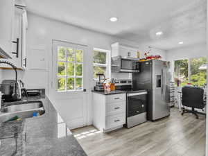 Kitchen with dark stone counters, stainless steel appliances, plenty of natural light, white cabinets, and recessed lighting