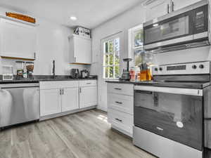Kitchen with stainless steel appliances, white cabinets, dark stone counters, light wood finished floors, and recessed lighting