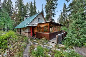Front view of house featuring a chimney, a deck, a metal roof, a standing seam roof, and a view of trees