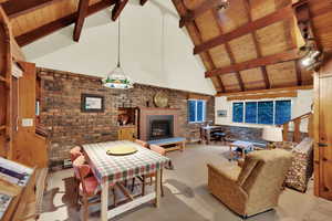 Carpeted living room featuring brick wall, high vaulted ceiling, a fireplace, and a wooden ceiling with exposed beams