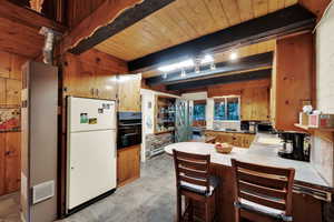 Kitchen featuring freestanding refrigerator, a peninsula, oven, a kitchen breakfast bar, and a wooden ceiling with exposed beams