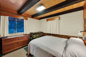 Bedroom featuring light carpet and a wood ceiling with exposed beams