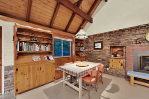 Dining area featuring brick wall, light carpet, wooden ceiling, and a glass covered fireplace