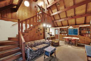 Living room with wood walls, stairway, a wood ceiling with exposed beams, carpet flooring, and high vaulted ceiling