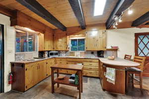 Kitchen with light countertops, decorative backsplash, stainless steel microwave, and a wood ceiling with exposed beams