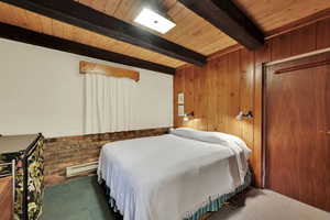 Bedroom featuring a baseboard heating unit, wooden walls, a wooden ceiling with exposed beams, and dark carpet