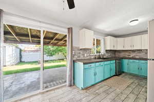 Kitchen with white cabinets, backsplash, wood finish floors, stainless steel dishwasher, and dark countertops