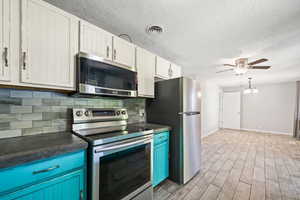Kitchen with stainless steel appliances, tasteful backsplash, a textured ceiling, ceiling fan, and wood tiled floors
