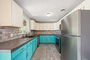 Kitchen featuring stainless steel appliances, dark countertops, white cabinets, blue cabinetry, and a textured ceiling