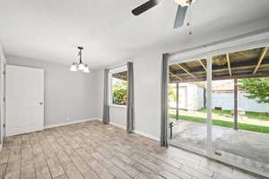 Spare room featuring light wood-style flooring, a chandelier, ceiling fan, and a textured ceiling