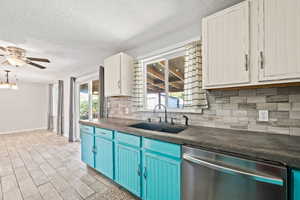 Kitchen with dark countertops, dishwasher, decorative backsplash, blue cabinets, and a textured ceiling
