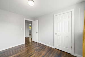 Unfurnished bedroom featuring dark wood-type flooring and baseboards