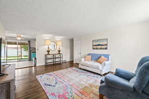 Living room with a textured ceiling, dark wood-style flooring, and ceiling fan