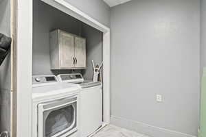 Washroom with washing machine and clothes dryer, light marble finish floors, and cabinet space