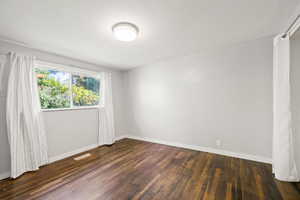 Unfurnished room featuring baseboards and dark wood-style floors