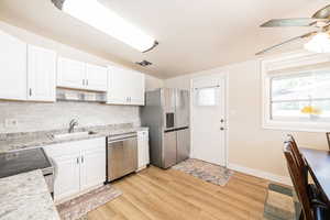 Kitchen featuring white cabinets, backsplash, appliances with stainless steel finishes, light wood finished floors, and ceiling fan