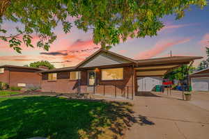Ranch-style house featuring an outbuilding, an attached carport, a lawn, brick siding, and a garage