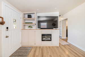 Unfurnished living room featuring light wood-style floors, a textured ceiling, built in shelves, and a glass covered fireplace