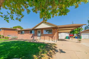 Single story home featuring an outbuilding, a carport, a front yard, and brick siding
