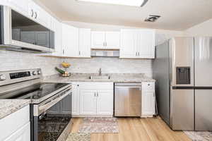 Kitchen featuring appliances with stainless steel finishes, white cabinets, light wood finished floors, tasteful backsplash, and vaulted ceiling