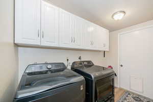 Laundry room featuring light wood-type flooring, washer and dryer, cabinet space, and a textured ceiling