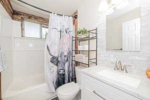 Bathroom with shower / bathtub combination with curtain, vanity, and backsplash