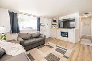 Living area featuring a textured ceiling, light wood-type flooring, and a glass covered fireplace