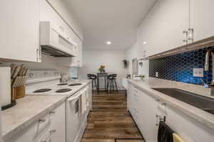 Kitchen featuring white appliances, white cabinetry, dark wood-style flooring, tasteful backsplash, and recessed lighting