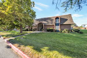 Front facade with brick siding, mansard roof, a front yard, and roof with shingles