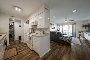 Kitchen featuring white appliances, open floor plan, white cabinets, estacked washer and dryer, and dark wood finished floors