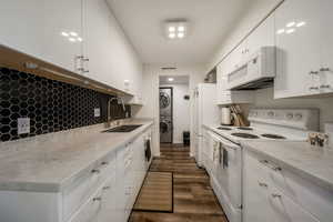 Kitchen with white appliances, dark wood finished floors, white cabinetry, stacked washing machine and dryer, and light stone countertops