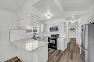 Kitchen with a peninsula, appliances with stainless steel finishes, light wood-style flooring, tasteful backsplash, and white cabinetry