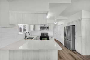 Kitchen with a peninsula, stainless steel appliances, light stone countertops, tasteful backsplash, and light wood-type flooring