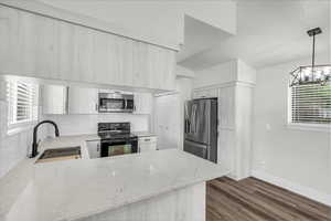 Kitchen with light stone counters, stainless steel appliances, tasteful backsplash, dark wood finished floors, and a peninsula