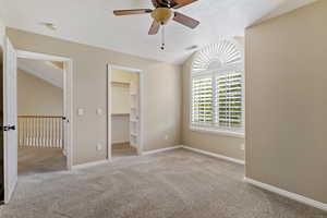 bedroom featuring light carpet, vaulted ceiling, a walk in closet, a ceiling fan, and a textured ceiling