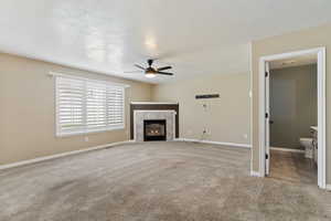 living room featuring light carpet, a tiled fireplace, a textured ceiling, and ceiling fan