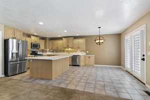 Kitchen featuring light tile patterned floors, appliances with stainless steel finishes, light countertops, a center island, and decorative backsplash