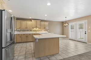 Kitchen with stainless steel fridge, light countertops, light tile patterned floors, tasteful backsplash, and a kitchen island