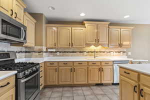 Kitchen featuring stainless steel appliances, light brown cabinets, decorative backsplash, light countertops, and light tile patterned flooring