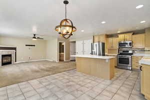Kitchen featuring light brown cabinetry, open floor plan, stainless steel appliances, pendant lighting, and tasteful backsplash
