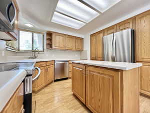 Kitchen featuring stainless steel appliances, light countertops, open shelves, a center island, and light wood-style flooring