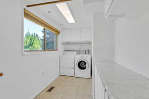 Laundry area with cabinet space, independent washer and dryer, and light tile patterned floors