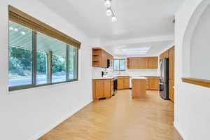 Kitchen with light countertops, open shelves, appliances with stainless steel finishes, light wood finished floors, and a kitchen island