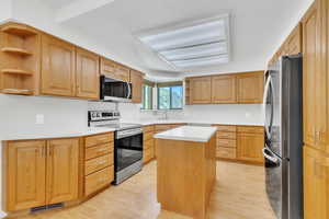 Kitchen featuring open shelves, appliances with stainless steel finishes, light countertops, light wood-style floors, and a center island