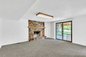 Unfurnished living room featuring a stone fireplace and carpet flooring