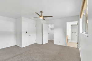 Unfurnished bedroom featuring light colored carpet, a spacious closet, and a ceiling fan