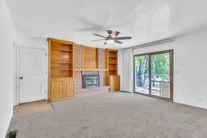 Unfurnished living room featuring a fireplace, carpet flooring, built in shelves, a textured ceiling, and a ceiling fan