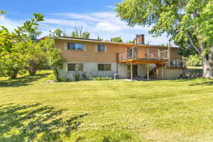 Back of property with a chimney, stairs, a lawn, a wooden deck, and brick siding