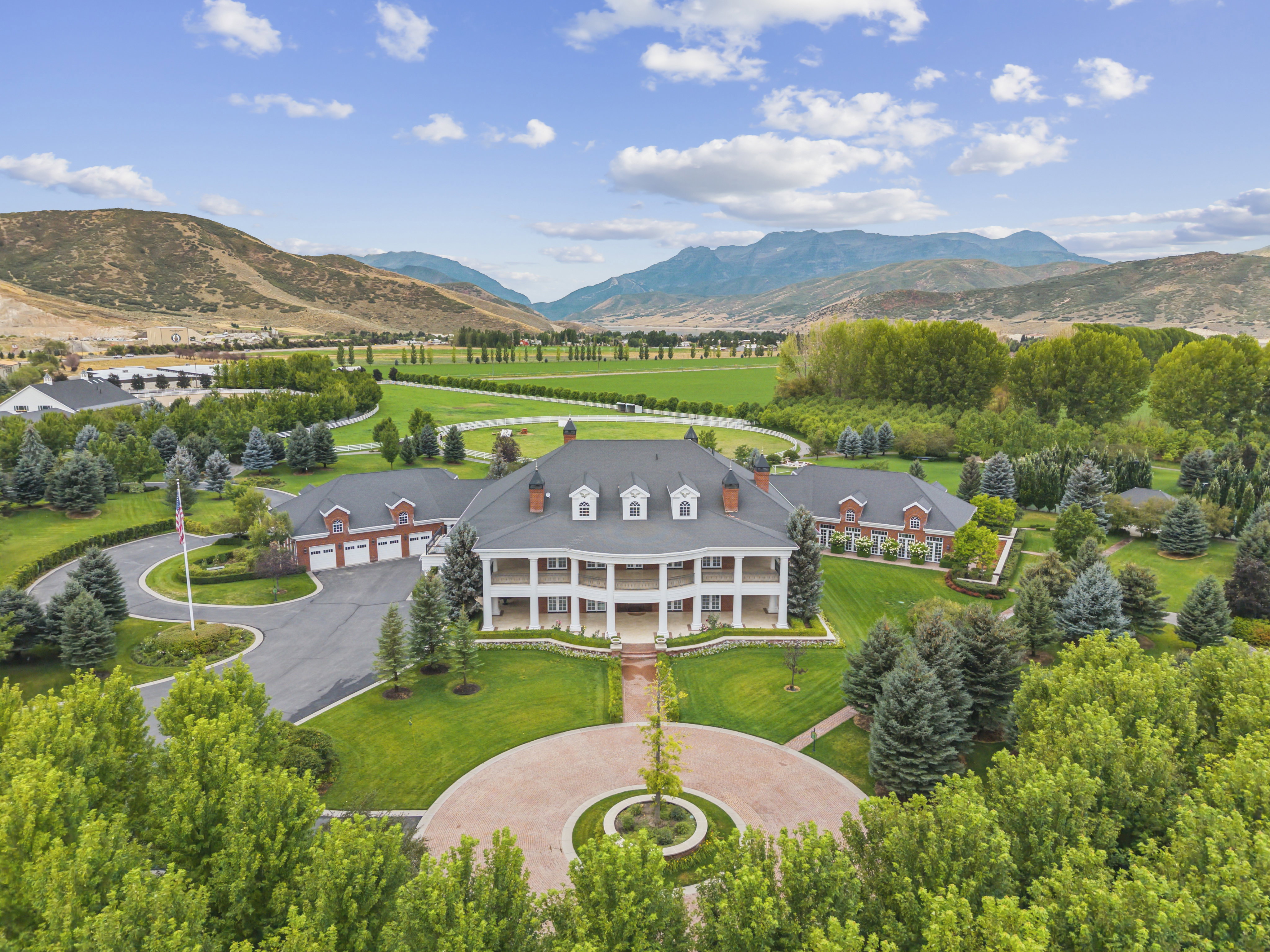 Colonial Revival estate with a grand circular driveway, extensive landscaping, mature trees, and mountain backdrop