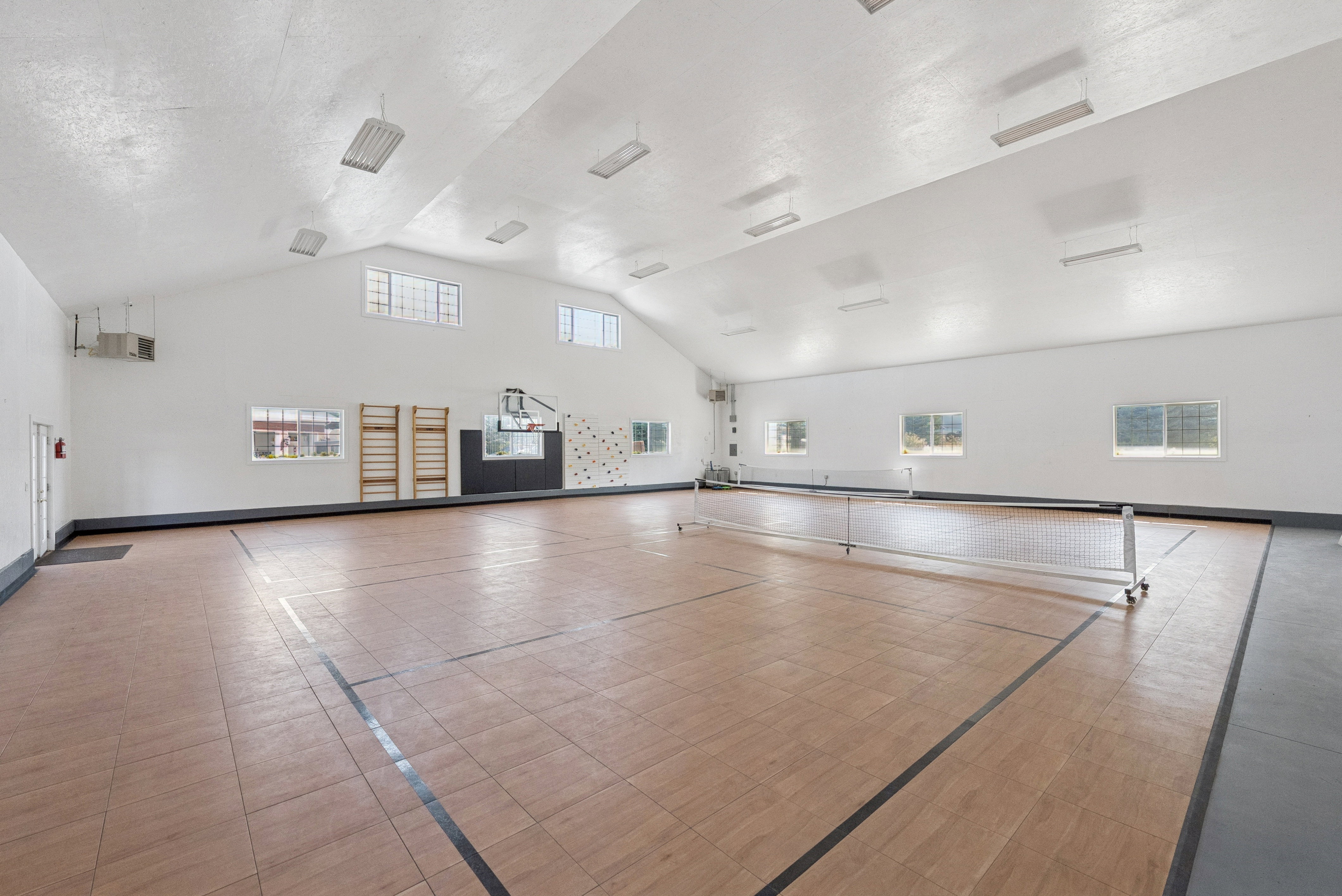 Spacious indoor court featuring wood-look flooring, multiple windows providing natural light, and a high vaulted ceiling